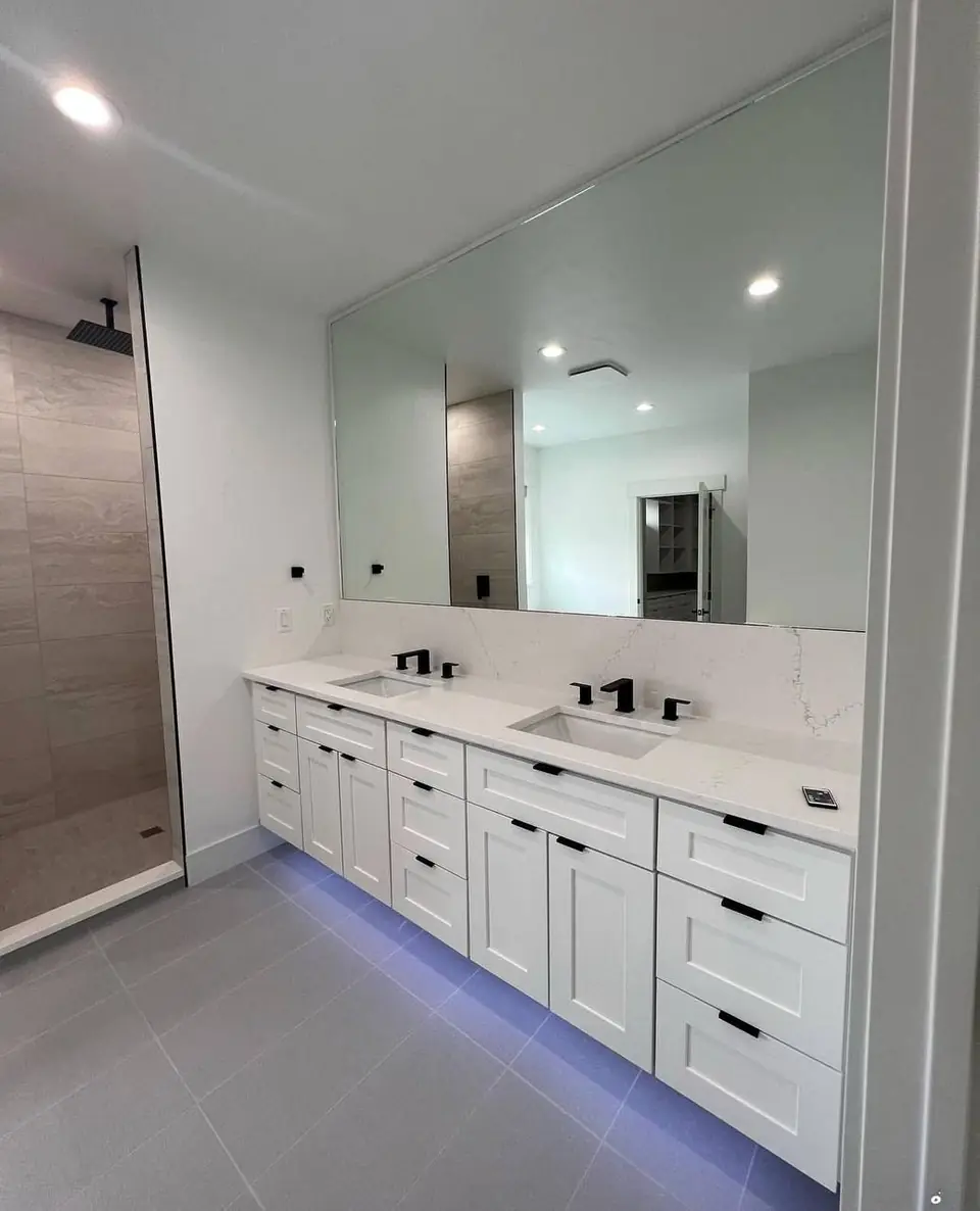 Primary bathroom with long white double vanity, wall-width mirror, under-cabinet lighting and tiled walk-in shower