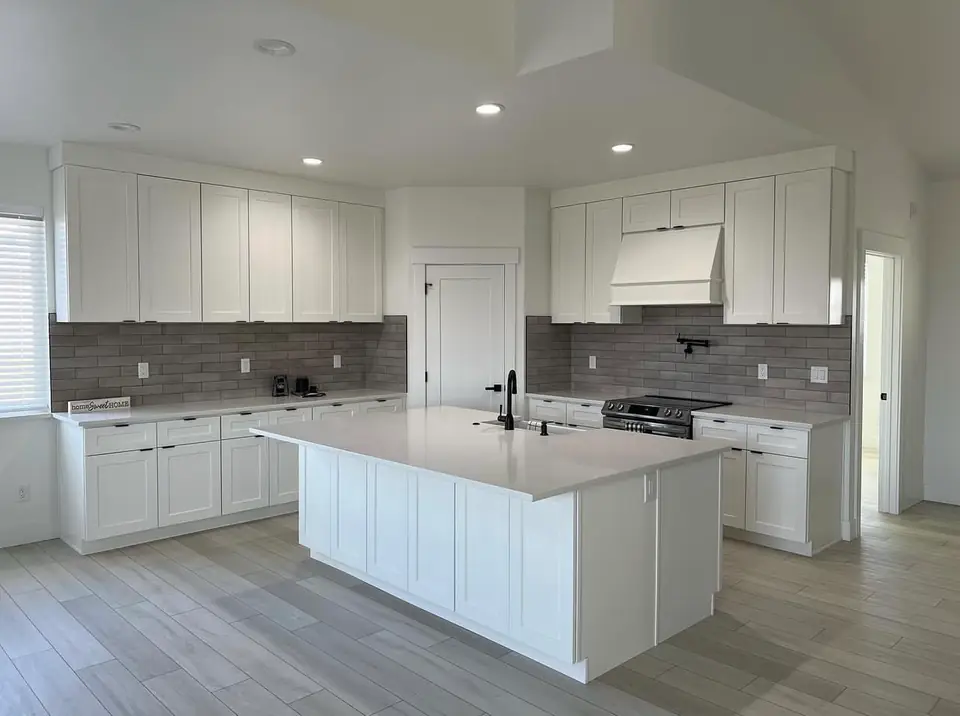Finished kitchen remodel with a large white island, white shaker cabinets and gray subway tile backsplash